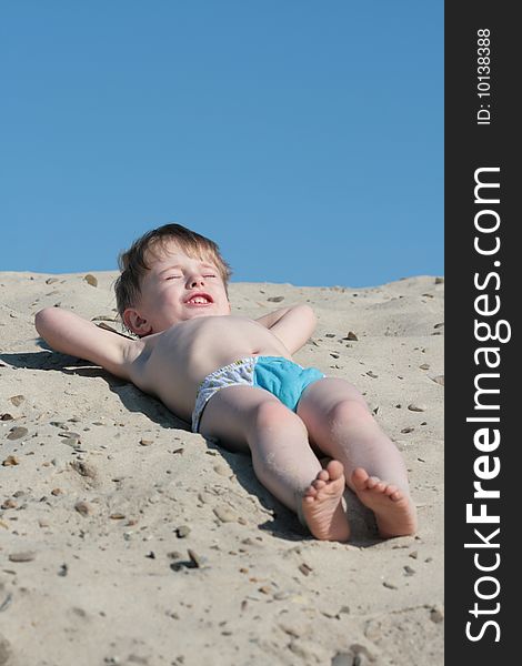 The little boy lays on sand of a beach. The little boy lays on sand of a beach
