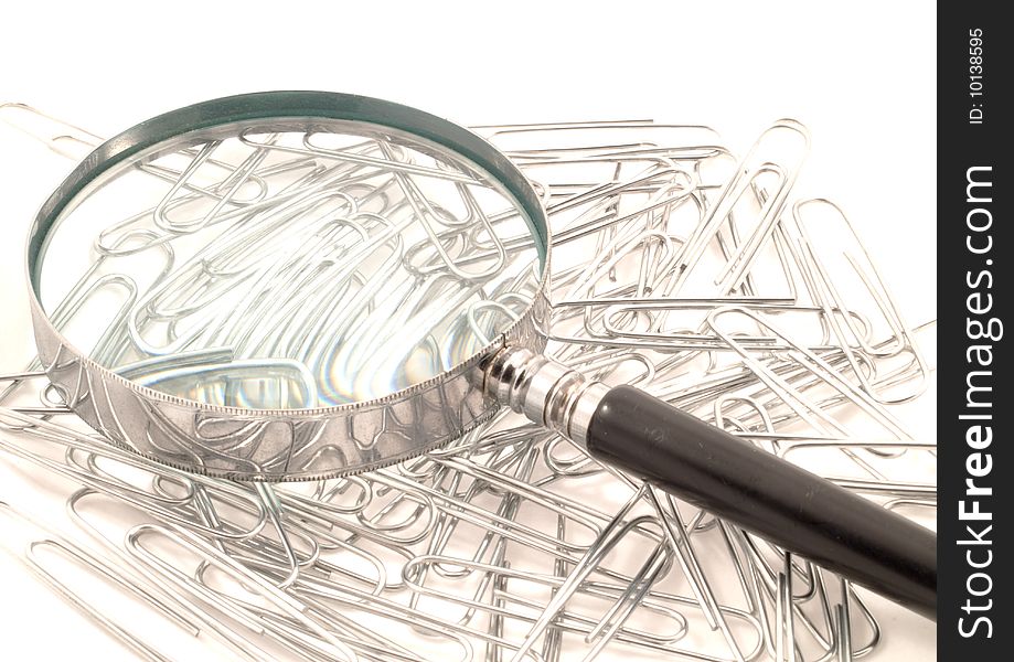 Magnifying glass on top of a stack of paperclips against a white background