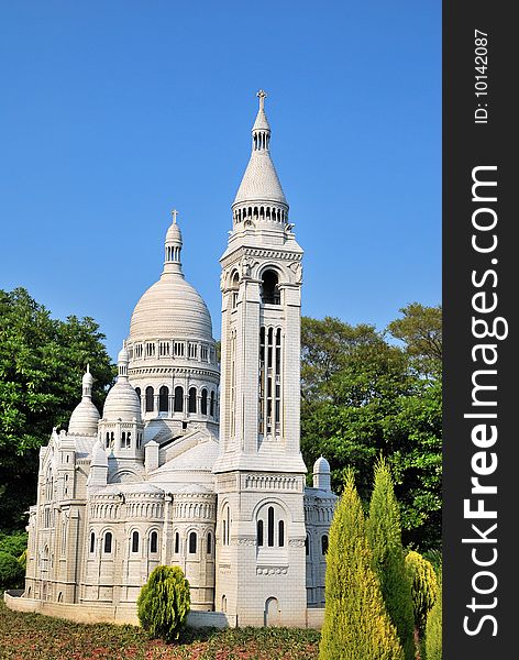 White, European style church architecture surrounded with nature with bird perched on roof