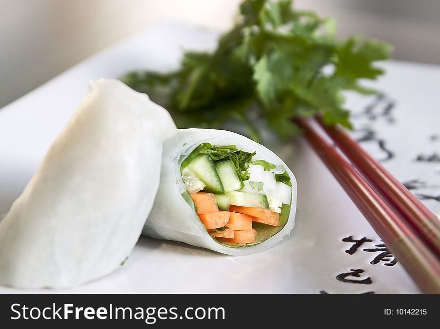 Springroll on a plate with chop sticks with greens in the background. Springroll on a plate with chop sticks with greens in the background