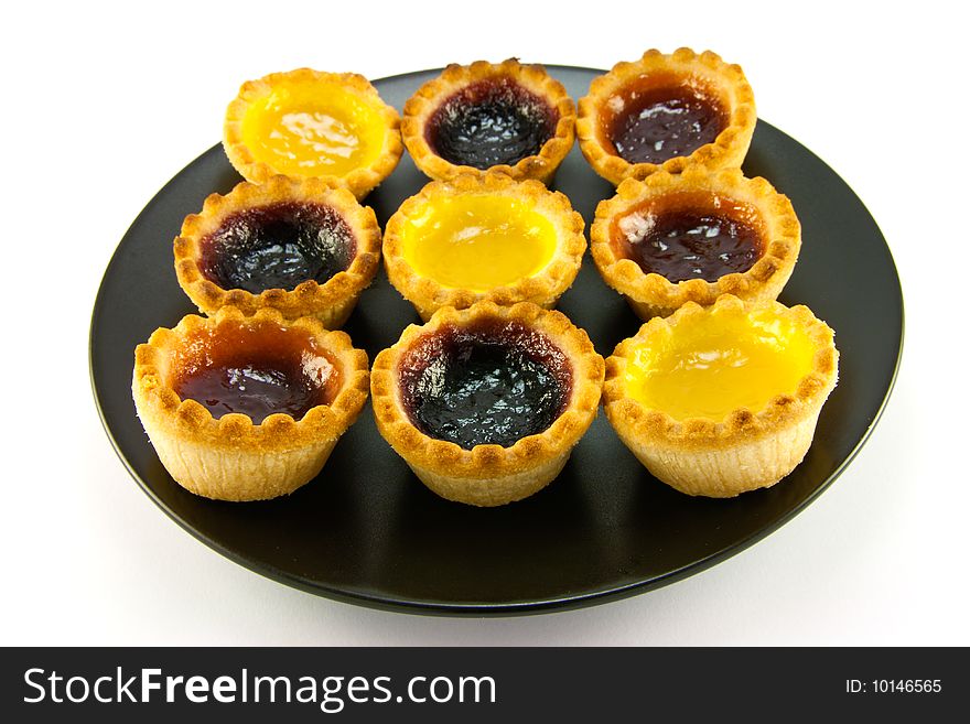 Selection red and yellow small jam tarts on a black plate with a white background