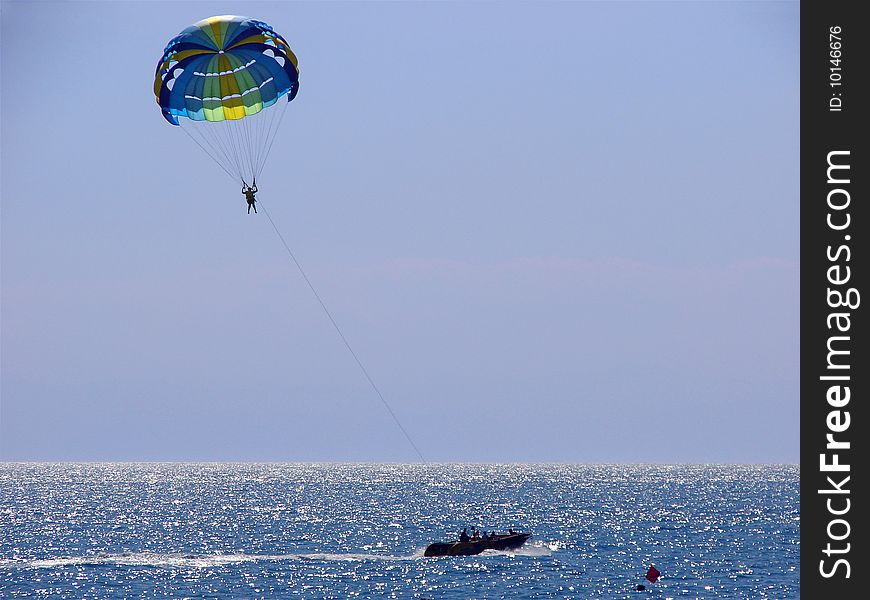 Woman flying on a parachute over the sea drived by boat