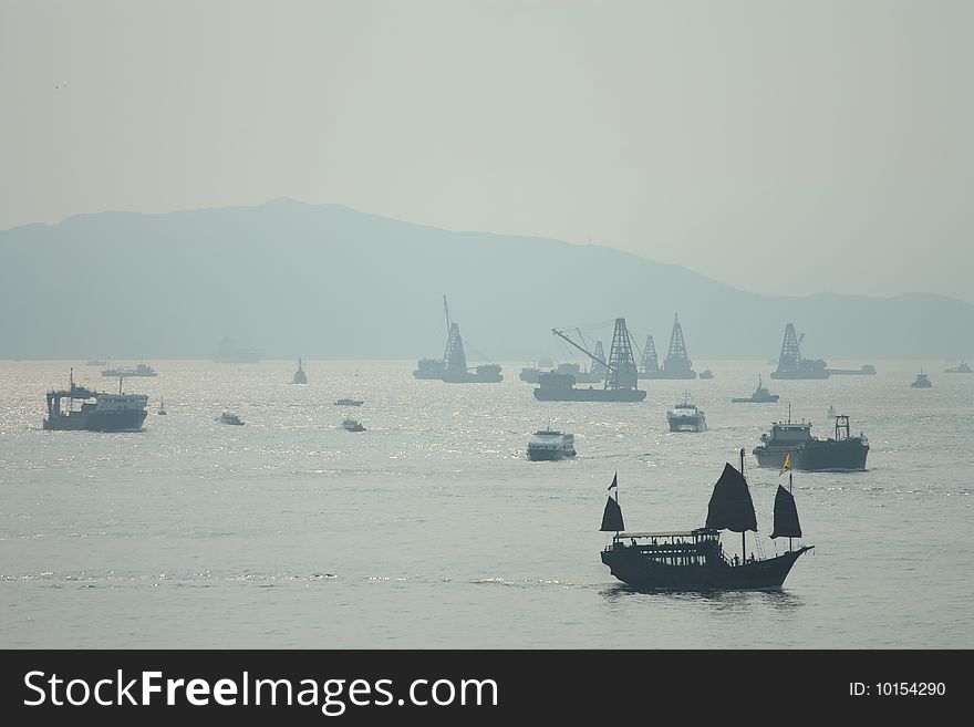 An old Chinese sailing boat sailing across a modern harbor. An old Chinese sailing boat sailing across a modern harbor.