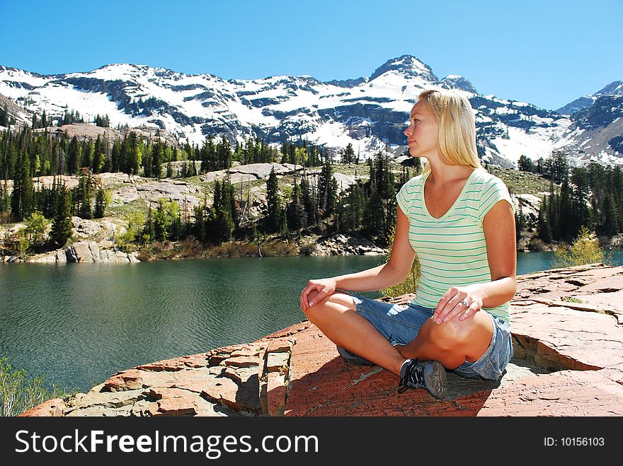 A woman sitting cross-legged next to a mountain lake. A woman sitting cross-legged next to a mountain lake.