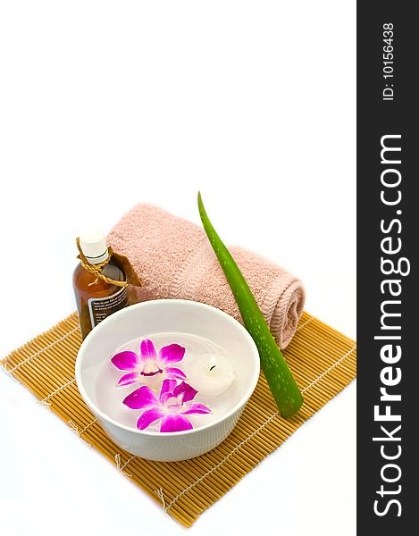 A white porcelain bowl with a tealight candle and two purple orchids floating in water, an aloe vera needle, a rolled up hand towel and a bottle of aromatherapy oil on a bamboo mat make up an assortment of items that are used in spas. A white porcelain bowl with a tealight candle and two purple orchids floating in water, an aloe vera needle, a rolled up hand towel and a bottle of aromatherapy oil on a bamboo mat make up an assortment of items that are used in spas.