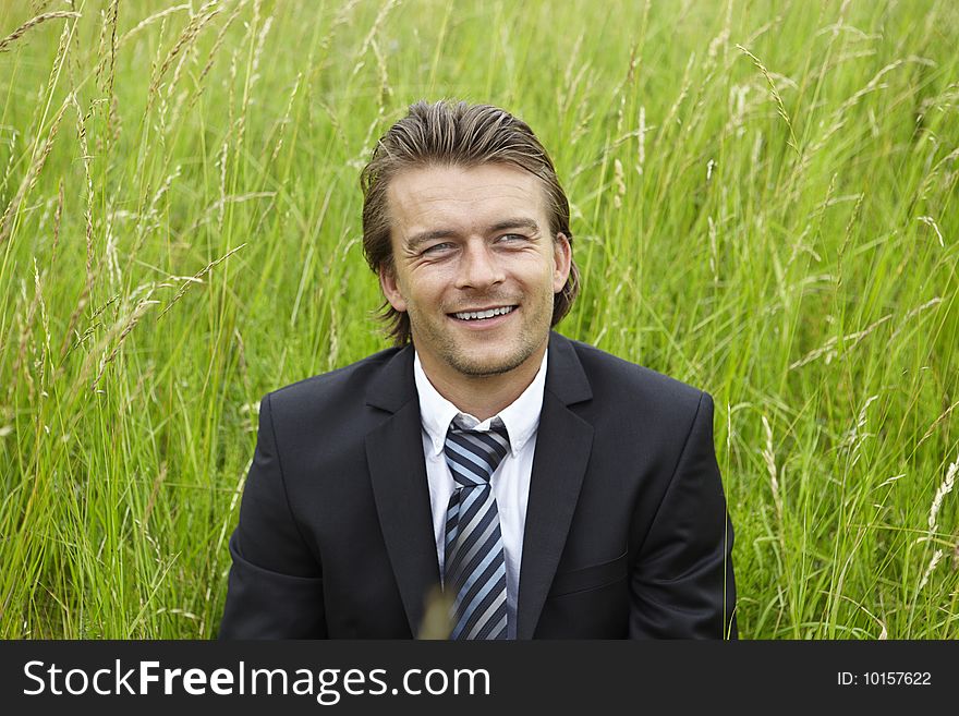 Smiling young businessman is sitting in a field
