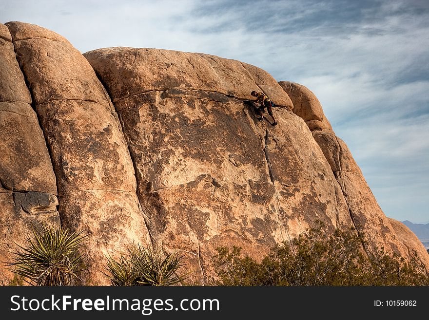 A rock climber making it to the top of a large rock at Joshua Tree National Park. A rock climber making it to the top of a large rock at Joshua Tree National Park.