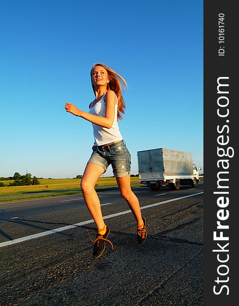 The woman running on road against the sunset sun