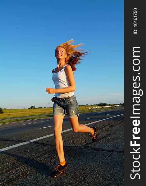 The woman running on road against the sunset sun