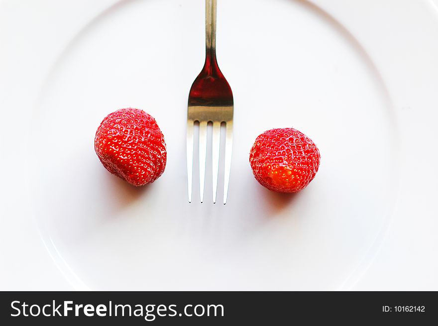 Fork among strawberry on the white plate