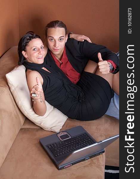 Young couple on the couch surfing the web with their laptop - showing a thumbs up sign. Young couple on the couch surfing the web with their laptop - showing a thumbs up sign.