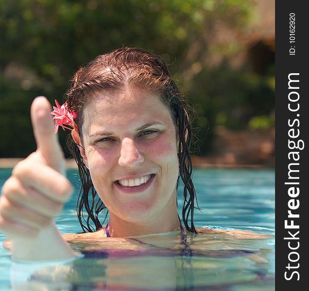 Young woman in a beautiful pool with palms in the background. She is showing a thumbs up sign. Young woman in a beautiful pool with palms in the background. She is showing a thumbs up sign.
