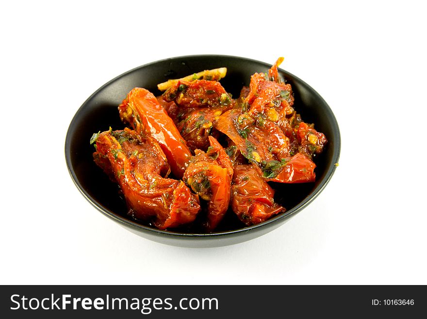 Pile of red sun dried tomatoes in a small black dish on a  white background