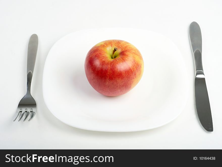 Fork, knife and red apple on white plate. Fork, knife and red apple on white plate