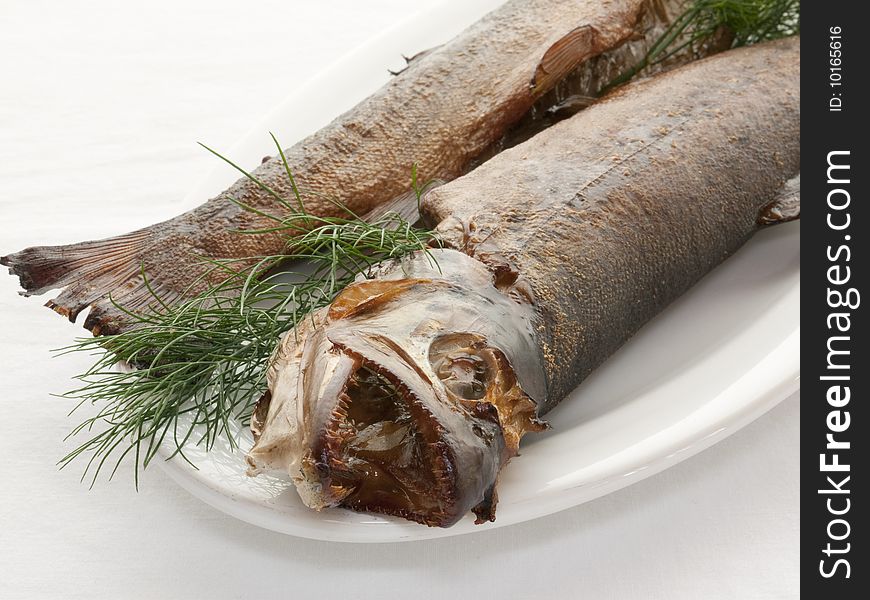 Two smoked trout on a white plate with a dill decoration