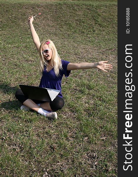 Happy girl with a laptop sitting on grass