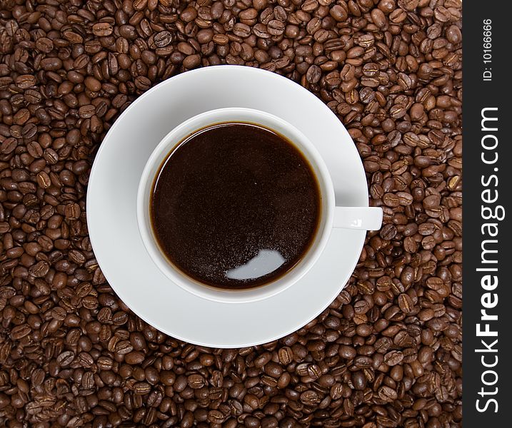 Cup of coffee sitting in a bed of coffee beans isolated over a white background