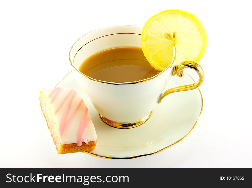 Tea in a cup and saucer with pink slice of cake and a slice of lemon on a white background. Tea in a cup and saucer with pink slice of cake and a slice of lemon on a white background