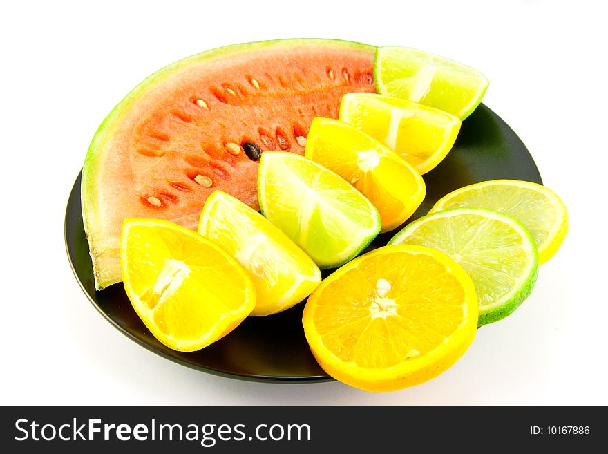 Slice of juicy red watermelon with lemon, lime and orange wedges and slices on a black plate with a white background. Slice of juicy red watermelon with lemon, lime and orange wedges and slices on a black plate with a white background