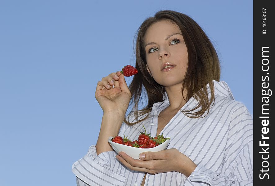 Pretty girl relaxing on balcony and eat red fresh strawberry.
