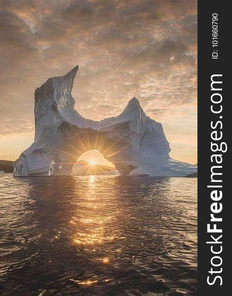 An iceberg and sunbeams glittering on the sea surface at sunset. An iceberg and sunbeams glittering on the sea surface at sunset.