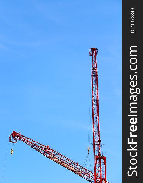 Fragment of a red construction crane with blue sky on background