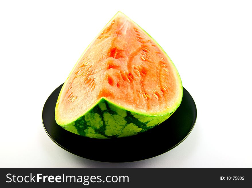 Slice of watermelon with green skin and red melon with seeds on a black plate with a white background. Slice of watermelon with green skin and red melon with seeds on a black plate with a white background