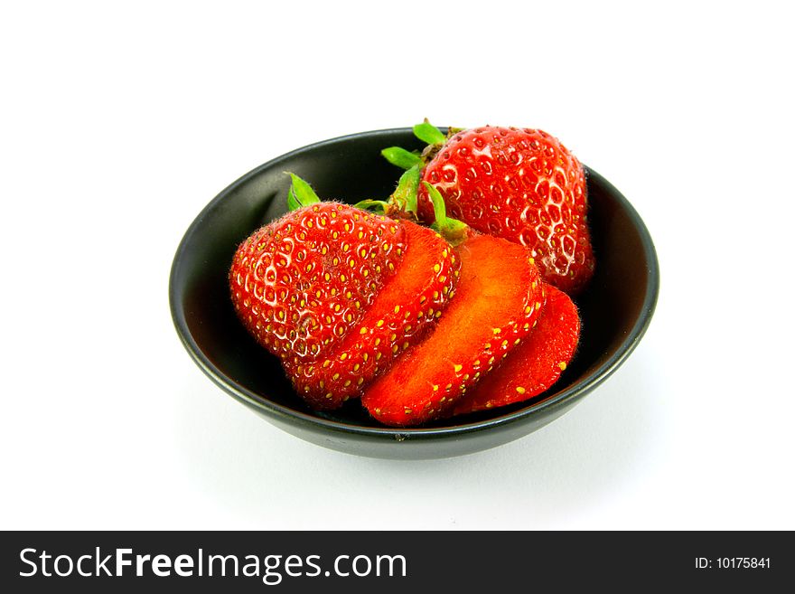 Sliced and whole red fresh strawberries in a small black dish on a white background
