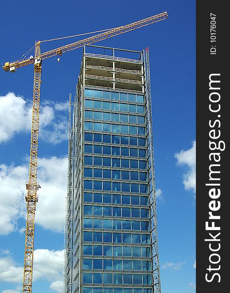 On a photo: Building and crane on a background of the blue sky.
