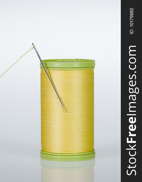 Needle threaded with yellow thread, stuck in a spool made of green plastic. Needle threaded with yellow thread, stuck in a spool made of green plastic.