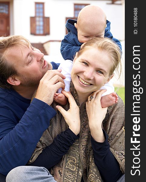 Beautiful happy family of three sitting on the grass laughing. Focus is on the mother. Beautiful happy family of three sitting on the grass laughing. Focus is on the mother