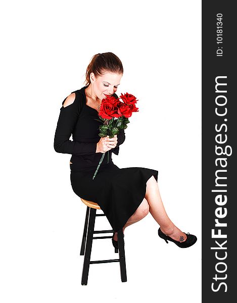 Young pretty woman, sitting on a bar chair and smelling the red roses in her hand, in an black dress for white background. Young pretty woman, sitting on a bar chair and smelling the red roses in her hand, in an black dress for white background.