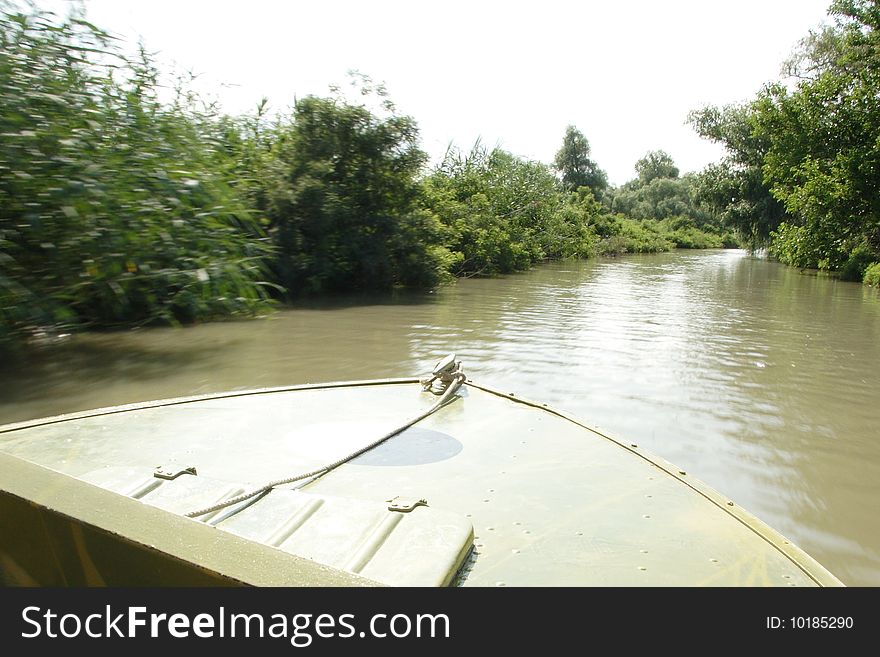 Baw of the motor boat sails down the river. The trees on the left part of the foto are blurred. Focus is under the boat's baw