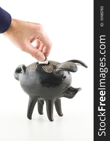 Male hand dropping a coin into a black piggy bank, white background.