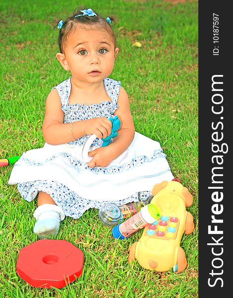 Little brunette girl with toys on green grass. Little brunette girl with toys on green grass.