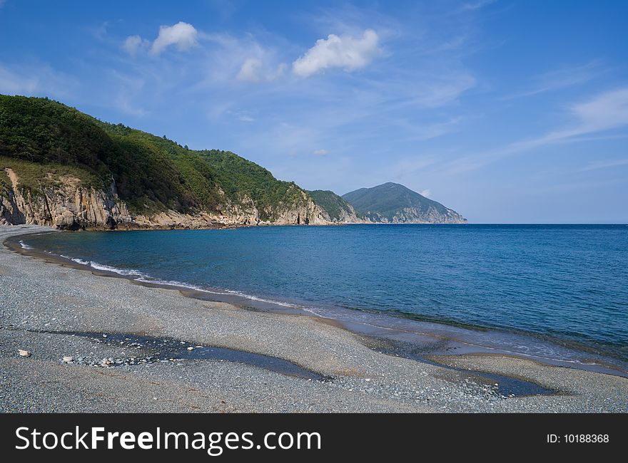 A landscape on Japanese sea. A beach with grey pebbles< green capes and cloudy sky. A landscape on Japanese sea. A beach with grey pebbles< green capes and cloudy sky.