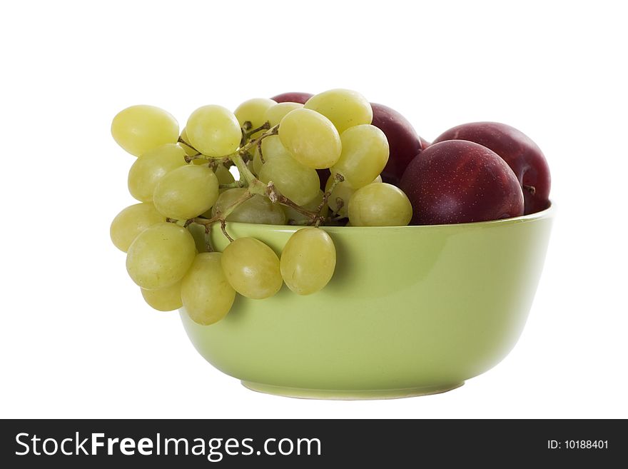 Isolated green bowl with red plums and green grapes. Isolated green bowl with red plums and green grapes