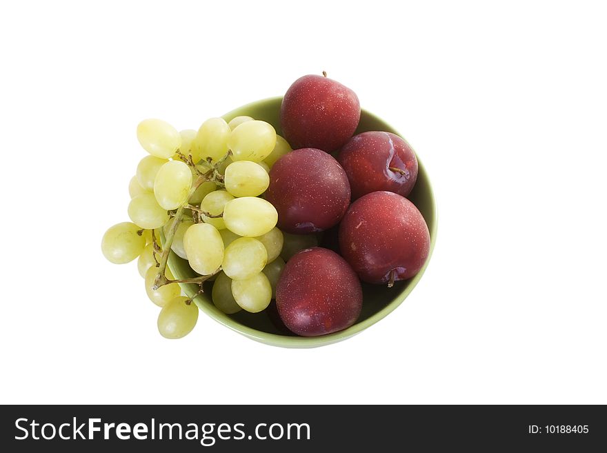 Green bowl with red plums and green grapes on white table. Green bowl with red plums and green grapes on white table.