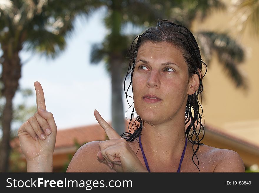 Young woman in a beautiful pool with palms in the background. She is pointing up.