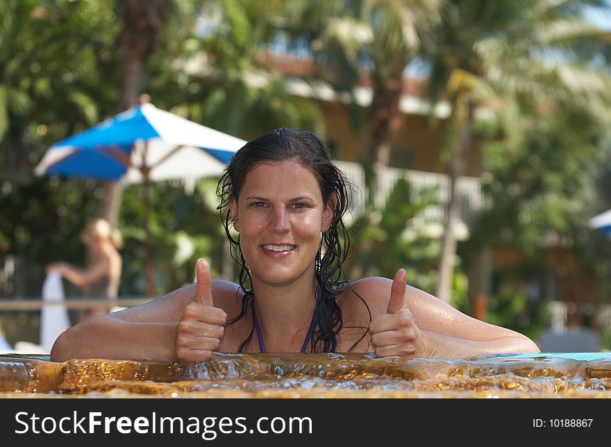 Young woman in a beautiful pool with palms in the background. She is showing a thumbs up sign. Young woman in a beautiful pool with palms in the background. She is showing a thumbs up sign.