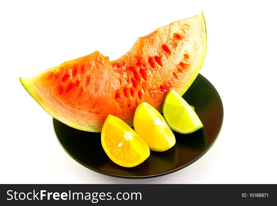 Slice of red juicy watermelon with a wedge of lemon, lime and orange on a black plate with a white background. Slice of red juicy watermelon with a wedge of lemon, lime and orange on a black plate with a white background