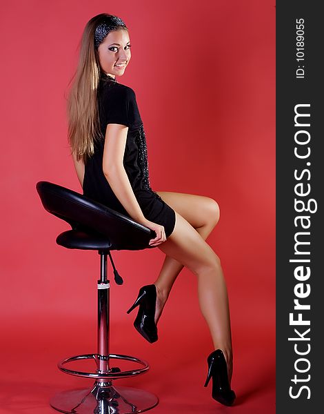 Beautiful young woman on a chair isolated on red