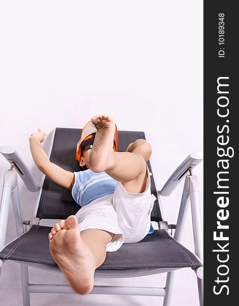 Picture of a little chinese boy wearing hat and sunglasses and resting on chair on vacation. Picture of a little chinese boy wearing hat and sunglasses and resting on chair on vacation