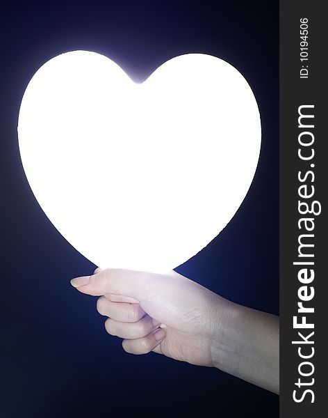 Bright heart in female hand with black background