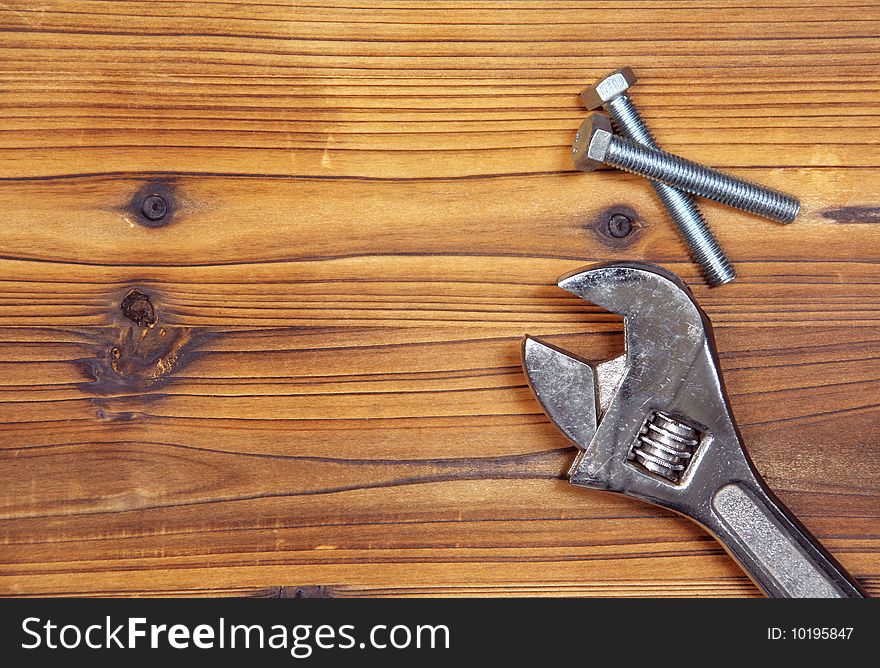 Screws and spanner on wood board.