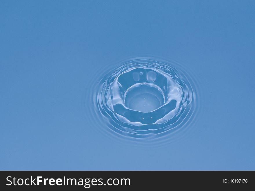 Water drop falling in water and creating a dip and ripples. Water drop falling in water and creating a dip and ripples