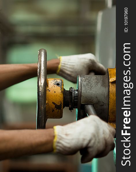 Control-wheel of old, worn industrial drilling machine with two gloved hands on the controls. Shallow depth of field with the wheel in focus and the hands blurred. Control-wheel of old, worn industrial drilling machine with two gloved hands on the controls. Shallow depth of field with the wheel in focus and the hands blurred.