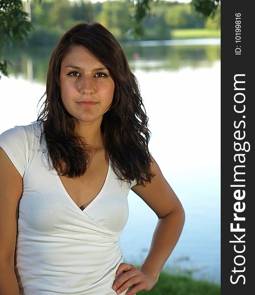 A beautiful young brunette woman standing by a serene lake with her hand on her hips. A beautiful young brunette woman standing by a serene lake with her hand on her hips.