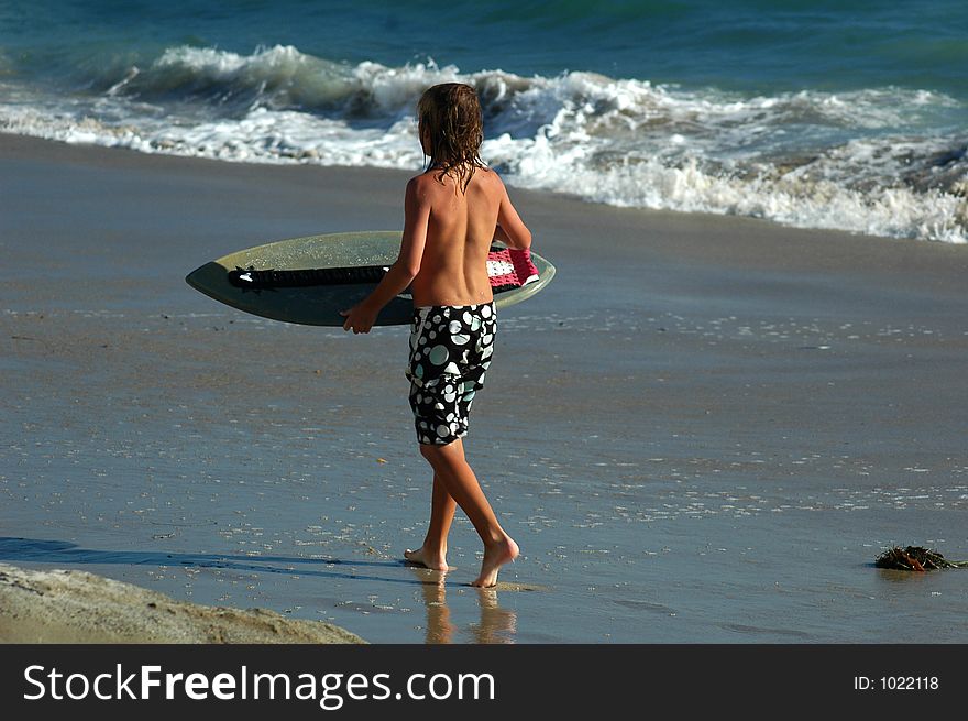 A boy with skim board  is walking ont the beach