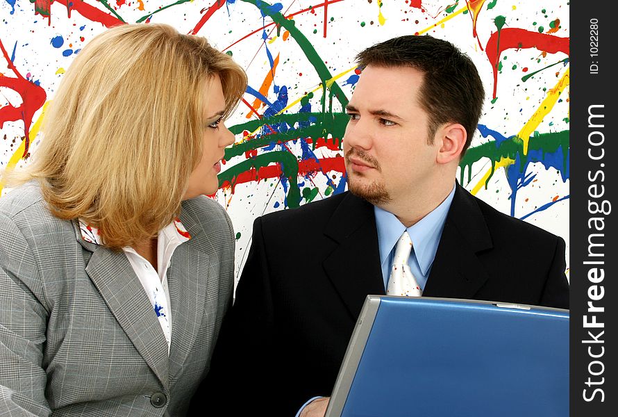 Professional woman and man with laptop exchange disapproving looks; paint splash background. Professional woman and man with laptop exchange disapproving looks; paint splash background